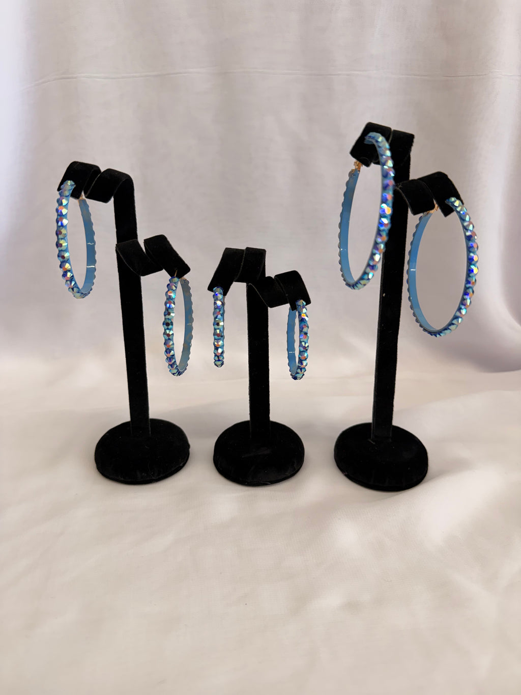 Aurora Collection Blue Zircon AB skinny hoop earrings for ballroom dance featuring iridescent teal Austrian crystals on a black display stand.