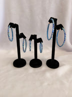 Aurora Collection Blue Zircon AB skinny hoop earrings for ballroom dance featuring iridescent teal Austrian crystals on a black display stand.
